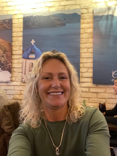 A smiling person taking a selfie in a room with scenic posters on the wall.