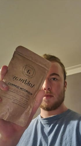 Person holding a brown package labeled 'Mushroom Gummies.'
